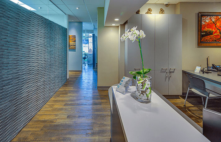 The image depicts a modern office interior with a long, sleek desk and a vase of flowers on it.
