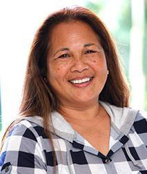 A smiling woman with long hair, wearing a plaid shirt, poses for the photograph.