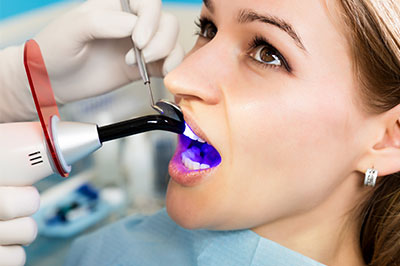 A woman receiving dental care with a device that appears to be using blue light.