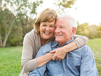 An elderly couple sharing a warm embrace in an outdoor setting.